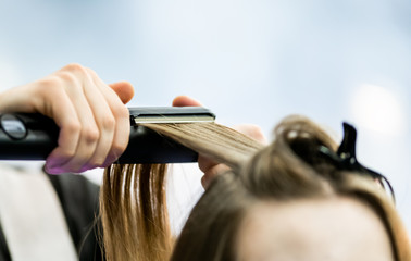 Professional hairdresser straightening long blond hair using straightener