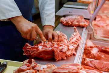 Hands of a butcher cutting slices of raw meat