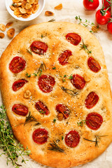 Italian traditional focaccia bread baking with with cherry tomatoes, parmesan and rosemary on light...