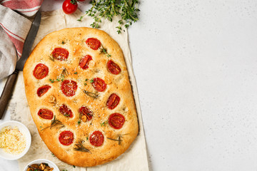 Italian traditional focaccia bread baking with with cherry tomatoes, parmesan and rosemary on light...