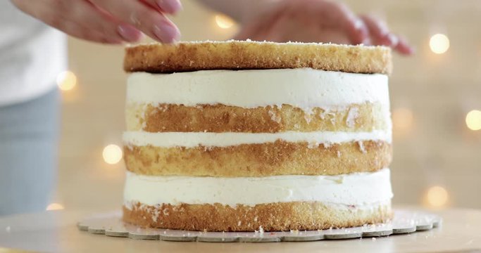 Confectioner woman is putting top sponge cake on cream making cake, hands closeup. Pastry chef is cooking homemade cake. Culinary, baking concept. Cream sponge cake with buttercream.