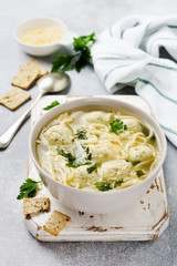 Soup with chicken meatballs and egg paste, Parmesan cheese, parsley in a ceramic bowl on a gray table background. Traditional Italian broth.  Top view.