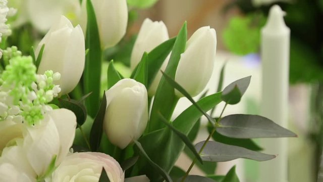 white tulips and candles with green leaves on the festive table close up