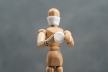 A wooden man in a surgical mask holds a tablet in his hand on a gray background.