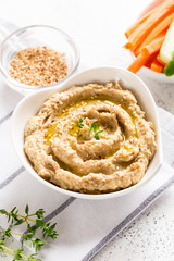 hummus sauce in a bowl, sesame seeds, olive oil, cucumber and carrots on a light background
