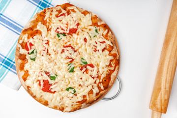 A vegetarian pizza sits on a round wooden Board next to a towel on a white table. The view from the top