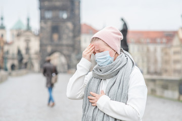 Woman wearing medical mask stands on Charles Bridge in Prague and checks her temperature....