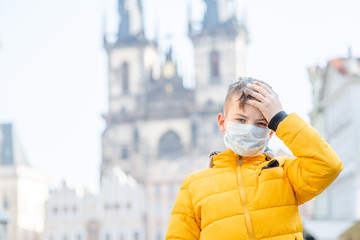 Boy wearing medical protective mask checks his temperature while stands  on the Old Town Square in Prague. Coronavirus epidemic concept. Empty space for text