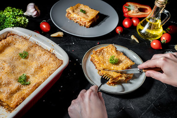 A hand take lasagna in plate with fork on the table on black background