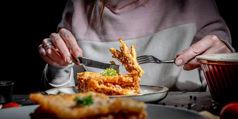 A hand take lasagna in plate with fork on the table on black background