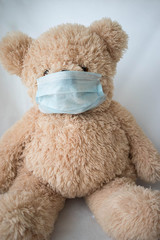 Quarantine, threat of coronavirus. Sad child and his teddy bear both in protective medical masks sits on windowsill and looks out window. Virus protection, pandemic, prevention epidemic.