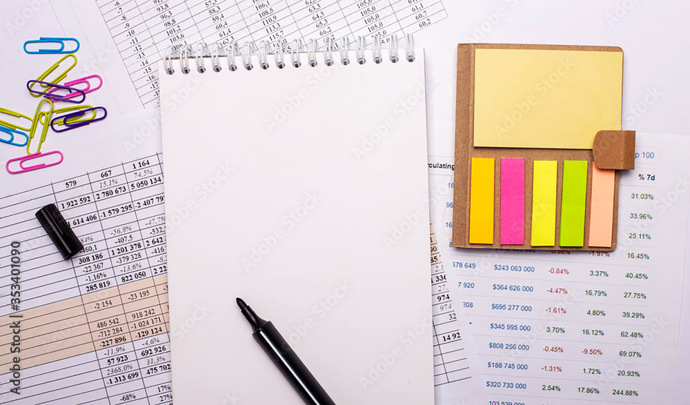 Poster notepad with marker, colored paper clips and bright note paper lies on the background of graphs. cop