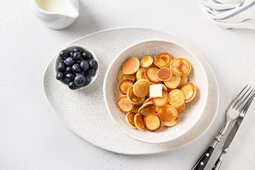 Homemade tiny cereal pancakes with blueberry on white kitchen table. View from above. Trendy child breakfast.