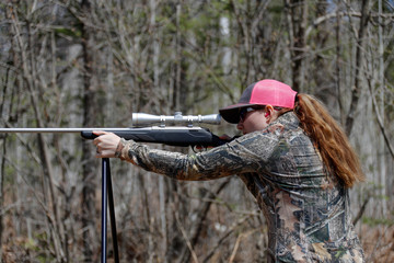 Woman shooting a rifle using shooting sticks.
