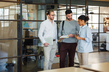 Photo of multinational focused colleagues talking and reading documents