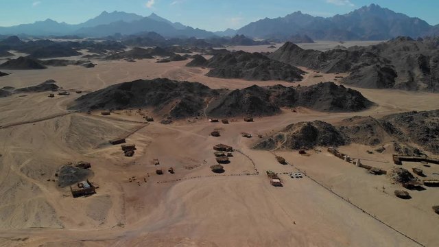 Top view of the Sahara desert, desert mountains. Wooden Bedouin houses. Sands. Tourists walk around the village.