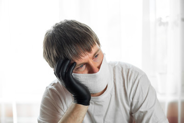 COVID-19. Self-isolation. Young caucasian man in a white mask, white t-shirt and black gloves...