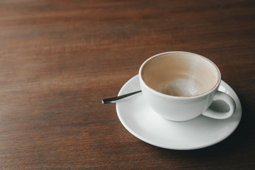 Empty cup of latte coffee with blot foam in white ceramic cup is placed on wooden vintage table with sun lighting in the morning after breakfast for relaxing, Selective focus shot with copy space.