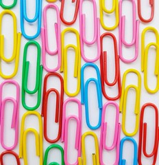 Multicolored metal paper clips on a white background.