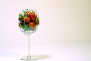 large strawberry in a wine glass on a light background with bright lighting close-up
