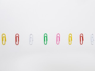 Multicolored metal paper clips on a white background.