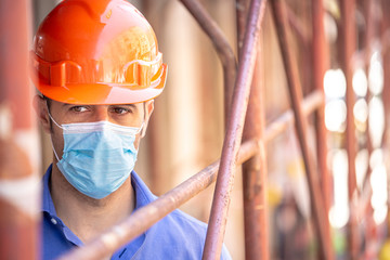 Ingegnere con casco arancio e camicia blu indossa una mascherina protettiva dentro un cantiere con...