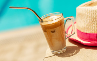 Summer holiday fashion concept banner - hat and cold coffee Frappe with metal recyclable straw next to swimming pool