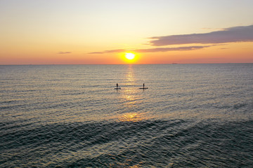 Stand up paddlers enjoy tropical island sunset in pacific ocean active couple stand up paddling...