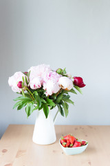 Bunch of Pink peonies in vase and strawberry on the wooden table . Flowers on a beige wooden table near the window. Home house interior. Beautiful peony flower.Summer day. Spring. Copy space