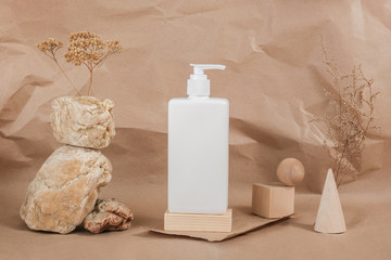 Cream, moisturizing lotion, shampoo or other cosmetic product in white blank bottle on stone, wooden geometric shapes and dried flowers on beige paper background. Beauty concept