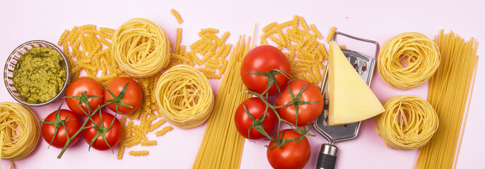 Variety of Types and Shapes of Dry Pasta Spaghetti Tagliatelle Fusilli Raw Tomatoes Bowl of Pesto Parmesan Cheese Top View Pink Background Long Italian Food