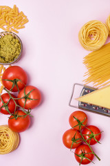 Variety of Types and Shapes of Dry Pasta Spaghetti Tagliatelle Fusilli Raw Tomatoes Bowl of Pesto Parmesan Cheese Top View Pink Background Vertical Italian Food