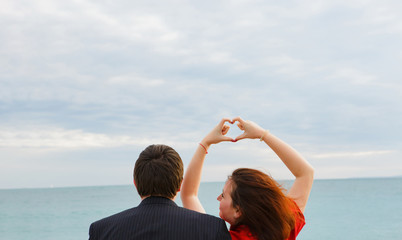 loving couple sitting on beach. spring seascape. heart of hand against the sky