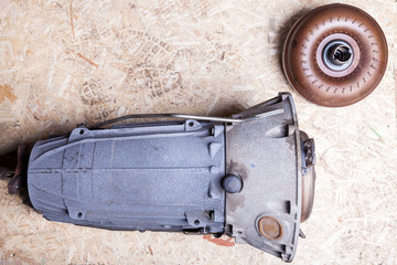 Separately, the car parts on the fiberboard sheet are an automatic metallic blue gearbox with a brown torque converter in the workshop for repair or for sale.