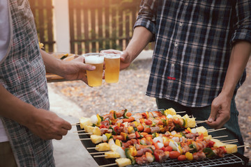 Young men cheers for a drink at a BBQ party between friends. Food, drink, people and family time concept.