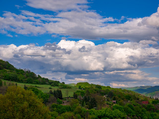 Massive clouds - Cumulonimbus - forming in the blue sky over hilly landscape