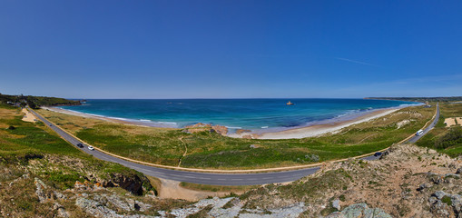 Fototapeta na wymiar Panoramic view of St Ouens Bay wth the FiVe Mile Road, part of the sand dunes, the beach with waves and sunny blue sky. Jersey, Channel Islands, uk