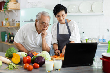 Fototapeta na wymiar Portrait of an elderly Asian couple. Tutorial Online cooking is in the kitchen at home. Senior couple watching video recipes on the laptop at the kitchen. The concept of leisure hobby of retirement