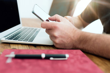close-up of man using smartphone in front of laptop computer in home office