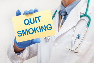 Close-up of a male doctor in gloves holding a sign with the text QUIT SMOKING