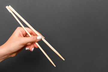 Creative image of wooden chopsticks in female hand on black background. Japanese and chinese food with copy space