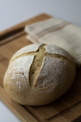 A loaf of homemade sourdough yeast bread boule with a simple cross style scoring technique on a wooden board. Dark and moody style.