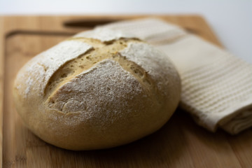 A loaf of homemade sourdough yeast bread boule with a simple cross style scoring technique on a wooden board. Dark and moody style.