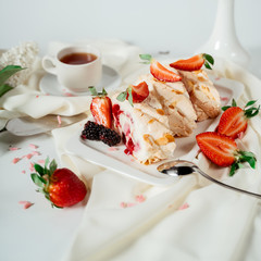 Fruit jam meringue cake garnished with hazelnut chips and strawberries, among lilac flowers. Food photography. Advertising and commercial close up design.