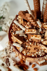 Chocolate cake decorated with various cookies and nuts on a glass plate standing on a white cloth. Food photography. Advertising and commercial close up design.