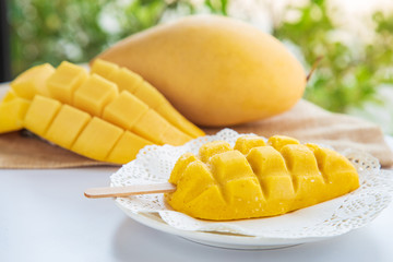 A mango ice cream stick on a white plate with mango fruit on white table background with nature...