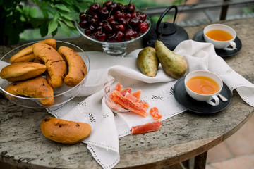 Tea ceremony, pouring tea from a teapot into a tea cup on a background of beautiful nature, fresh cherry and croissant. Hot cup of tea on rustic table. 