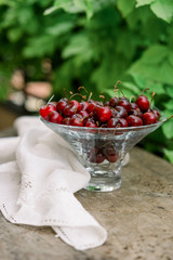 Cherries in Glass bowl. Red cherry & leaf in bowl on wooden background with sunlight. Fresh cherries bowl as healthy fruitarians concept. Sweet organic berries on old rustic stump. Juicy tasty fruit