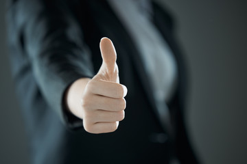 Thumbs up from girl. Business concept of success against the background of suit in blur.