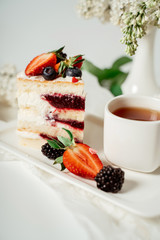 Sliced white berry cream cake decorated with strawberries and blackberries, among lilac flowers and green leaves. Food photography. Advertising and commercial close up design.